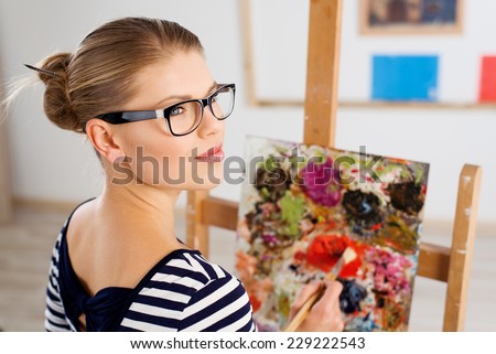 Young female artist with color palette and brush in studio. Attractive woman painter thinking of drawing new picture.