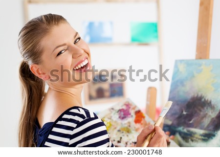 Happy smiling artist woman painting on canvas with acrylic colors. Young lovely Caucasian female applying new painting technique on her picture.