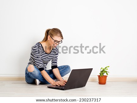 E-commerce. On-line woman customer buying in front of laptop sitting at white wall in her house.