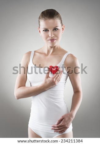 Smiling female holding red heart at breast. Heart protection and examination concept.