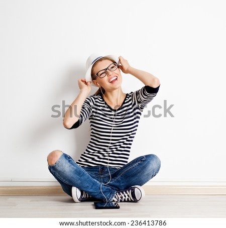 Stylish pretty woman in hat listening music in headphones on the floor of empty room. Youth and lifestyle concept.