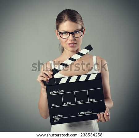 Film production and media. Scene tryout. Pretty smiling female with clapperboard over grey background.