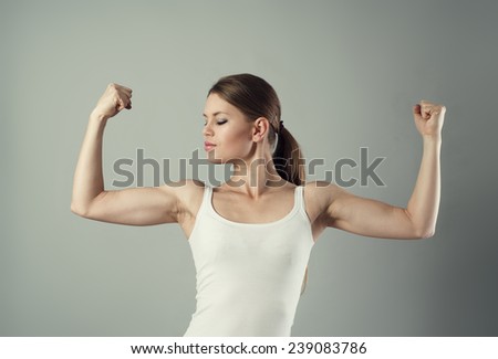 Close-up portrait of young sporty female showing her biceps. Concept of power and strength.