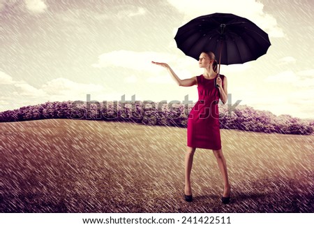 Pretty young business woman standing with umbrella in the rain. Concept of crisis protection and risk insurance.