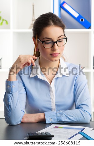 Young female bookkeeper calculating company\'s profit and loss. Attractive woman financial analyst sitting over documents at workplace.