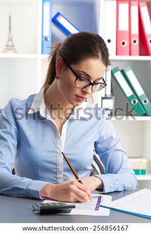 Female financial director singing contract in the office. Pretty businesswoman sitting at the table with ballpoint and calculator.