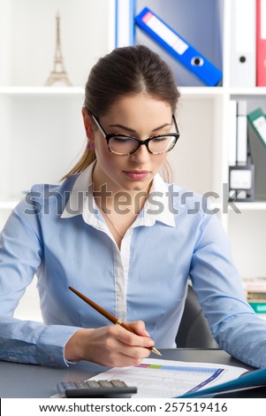 Female financial controlling expert planning annual budget sitting at her desk. Young concentrated woman professional working in the office.