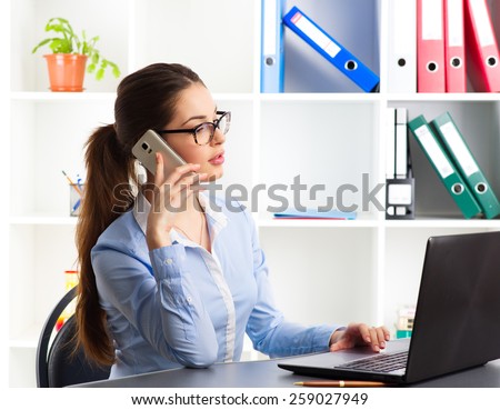 Young business woman agent using laptop and cell phone in the office. Portrait of real estate expert communicating with clients.