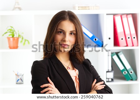 Close-up of pretty smiling woman expert wearing business suit. Young successful marketing manager standing in the office over folder shelves background.