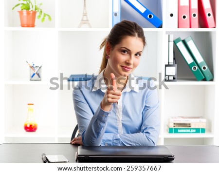 Portrait of smiling businesswoman loan agency expert showing thumb up. Amiable female manager sitting at the desk with laptop and phone.