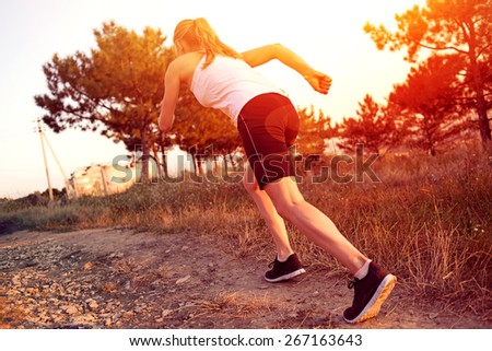 Young woman jogger running on the road in morning park. Active female athlete during outdoors workout at sunset.