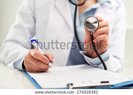 Closeup of doctor physician reporting medical test results. Woman medic in uniform filling health insurance document in the office.  Shallow depth of field.