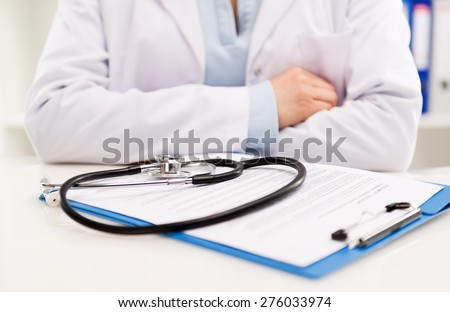 Close up of female doctor sitting at her desk with stethoscope and medical form. Medical treatment and health care. Shallow depth of field.