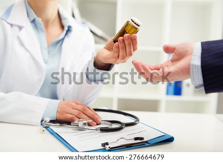 Closeup of female physician giving medicine bottle to patient. Doctor visit and treatment concept. Shallow depth of field.