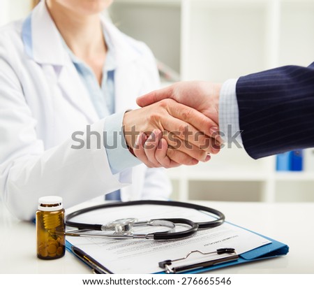 Woman doctor and businessman shaking hands in medical office. Concept of help, support and assistance. Shallow depth of field.