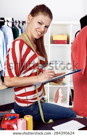 Portrait of happy smiling female self-employed working in own fashion studio. Young creative clothing designer drawing a sketch of new dress.
