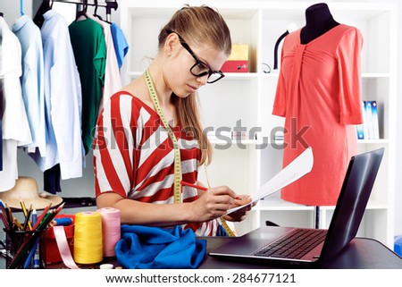 Fashion designer drawing costume draft at her workplace in studio. Woman dressmaker sketching using laptop computer.