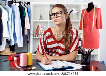 Clothing stylist thinking of new fashion dress design drawing template at the desk. Young successful female atelier owner creating trendy clothes.