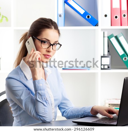 Businesswoman with phone working at computer in the office. Female real estate broker consulting customer online.