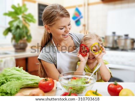 Smiling mummy and her cute daughter having fun cooking vegetarian dinner. Little child playing with colorful pepper rings while preparing salad with mother.