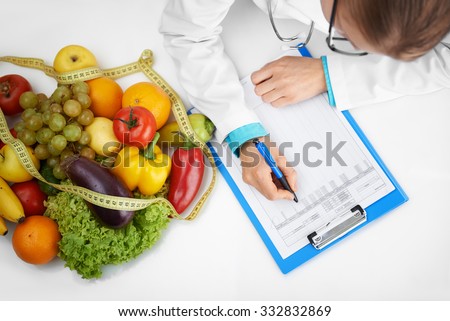 Doctor therapist writing case development form sitting at the desk in hospital. Female nutritionist prescribing diet to patient.