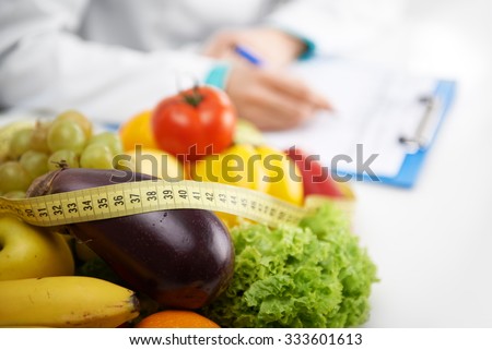 Healthy nutrition concept. Close-up of fresh vegetables and fruits with measuring tape lying on doctor\'s desk.