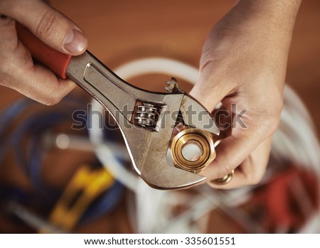 Close-up of plumber hands screwing nut of pipe with wrench over plumbing tools background.  Concept of repair and technical assistance.