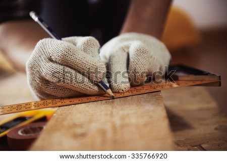 Construction work. Woodwork. Male builder marking point on plank sitting on the floor.