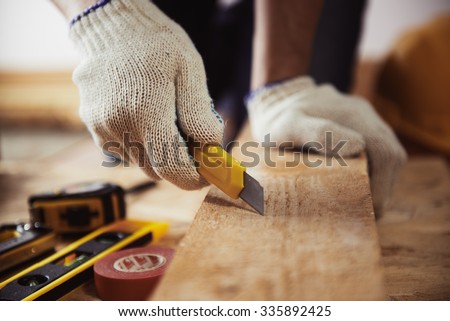 Male contractor working with wooden plank and cutter on the floor. Close-up of mature craftsman's hands in protective gloves with building tools.