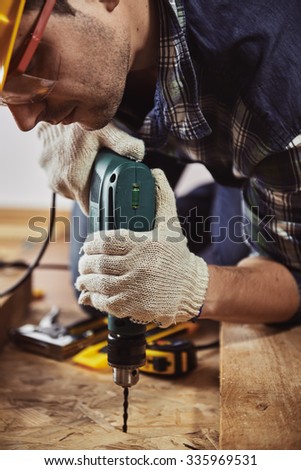 Male carpenter with drilling instrument working at home on the floor. Concept of house improvement and renovation.