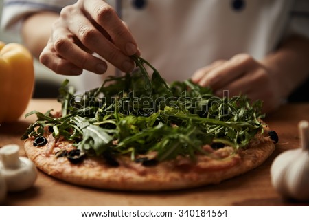 Close-up of woman chef making vegetable pizza on wooden board with pepper, mushrooms, garlic.