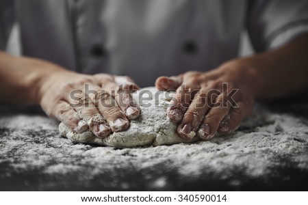 Close-up of woman baker hands kneading the dough on black board with flour powder. Concept of baking and patisserie.