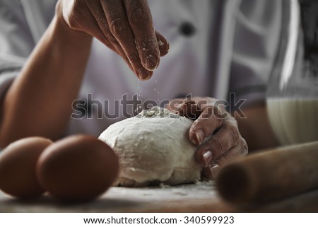 Female in chef uniform adding flour to dough preparing pizza in the kitchen. Cookery and healthy nourishment concept.