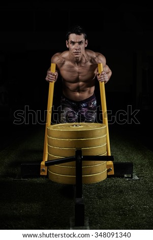 Strong man with muscular body pushing iron sled with weight in the gym. Cross fit and weightlifting.