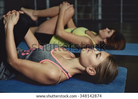 Group of women making pilates lying on yoga mats in aerobics class. Young sporty Caucasian girls stretching legs on the floor in gym.