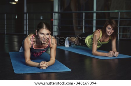 Smiling women doing core exercise for abdominal muscles and forearm. Yoga class in the gym.