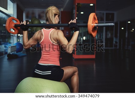 Back view of slim athletic woman with muscular body holding barbell exercising in gym. Concept of strength, health and endurance.