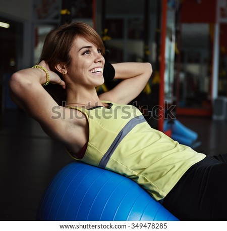 Happy young woman training abdominal muscles on fit ball in aerobics class. Body improvement and care concept.