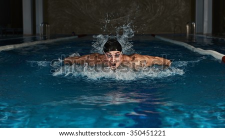 Butterfly swimmer wearing cap and goggles taking breath. Muscular athlete training indoors in the pool.