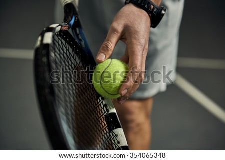 Close-up of male hand holding tennis ball and racket. Professional tennis player starting set.