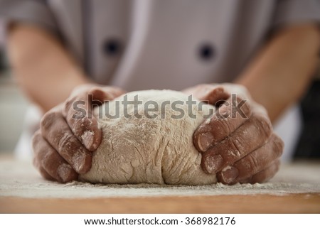 Woman chef with raw dough. Young female in uniform preparing bread dough on wooden table.