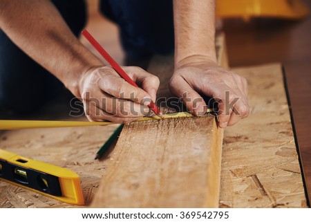 Craftsman measuring wooden plank with ruler on the floor. Concept of diy, woodworking and home renovation.