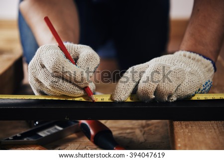Close-up of craftsman hands in gloves measuring wooden plank with ruler and pencil. Concept of carpentry and construction.