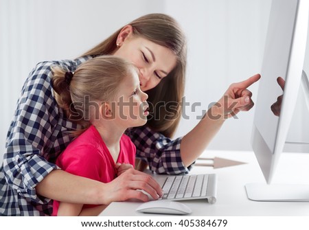 Young family shopping online. Pretty smiling mom pointing at the screen showing something to her small daughter.
