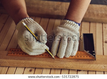 Close-up of male carpenter hands drawing mark on wooden flooring with ruler and pencil. DIY concept.