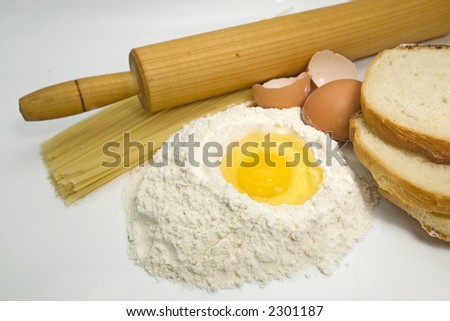 Egg in a pile of flour with pasta, bread and kitchen tools for cooking