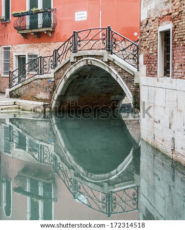 A Perfect Reflection Of The Bridge In The Water Of The Old Canal - Venice, Italy