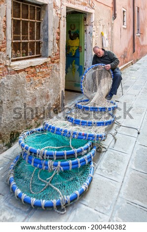 VENICE, ITALY - 06 MARCH, 2014: Fisher darning fishing nets on the narrow Venetian street