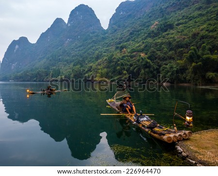 XINGPING, CHINA - OCTOBER 20, 2014: Cormorant fisherman sits on the ancient bamboo boat with a lighted lamp in his hands - The Li River, Xingping, China