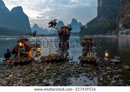 XINGPING, CHINA - OCTOBER 21, 2014: Cormorant fisherman on the ancient bamboo boat with a lighted lamps and cormorants - The Li River, Xingping, China